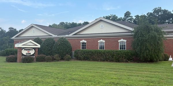 Brick medical building with a sign reading 'Priority Care' surrounded by greenery.