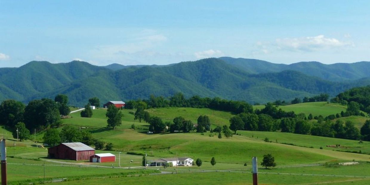 Rolling green hills and farms with a backdrop of blue mountains under a clear sky.