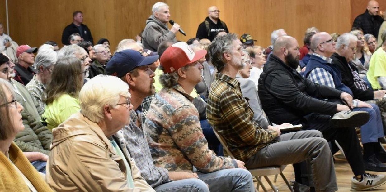 Community meeting with attentive attendees and a speaker holding a microphone.