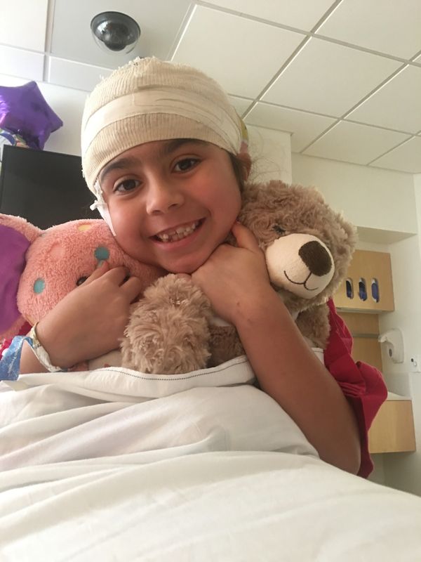 Smiling child with head bandage hugs teddy bears in hospital.