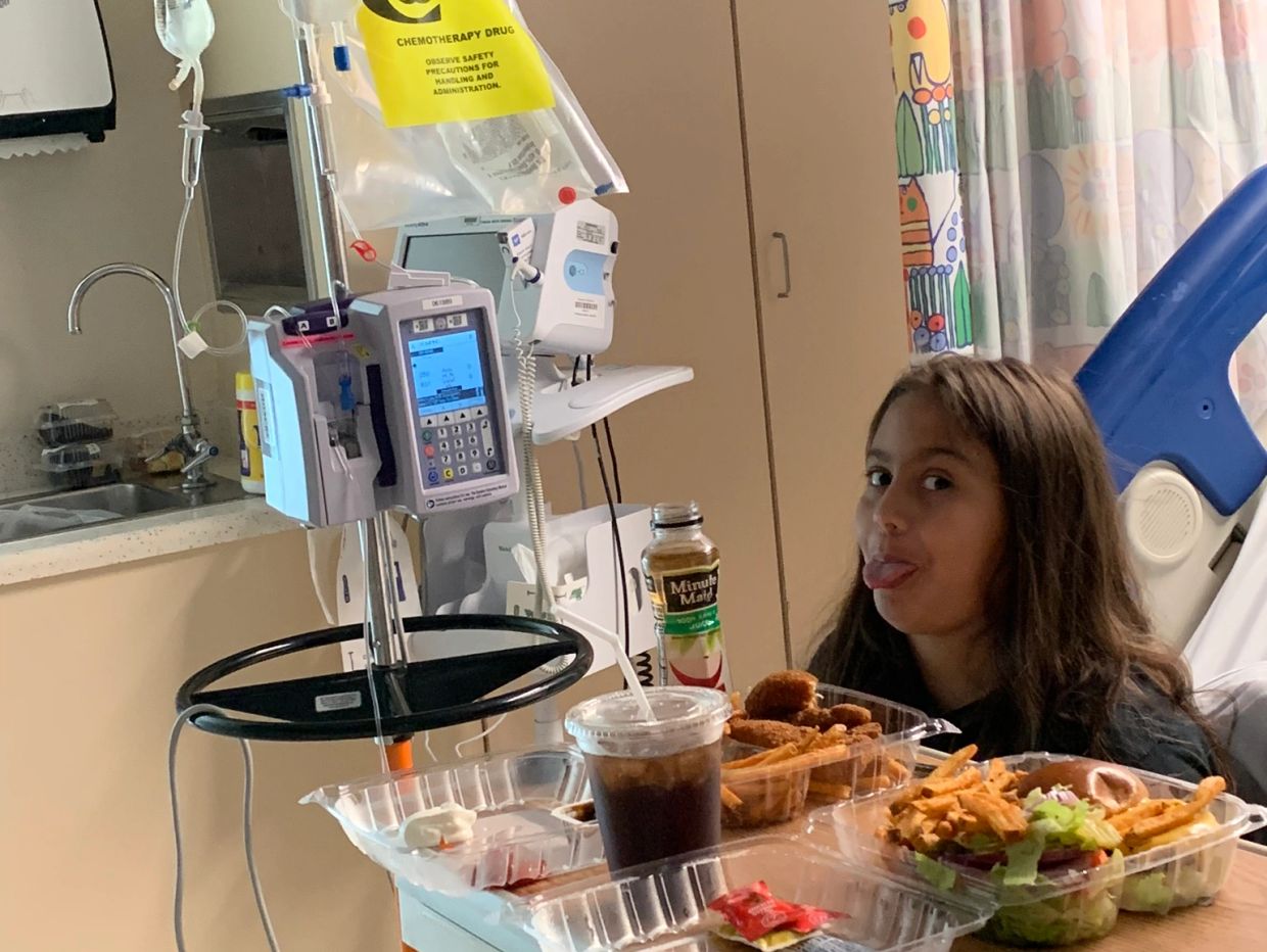 Young girl in hospital bed with chemotherapy drip and meal tray.