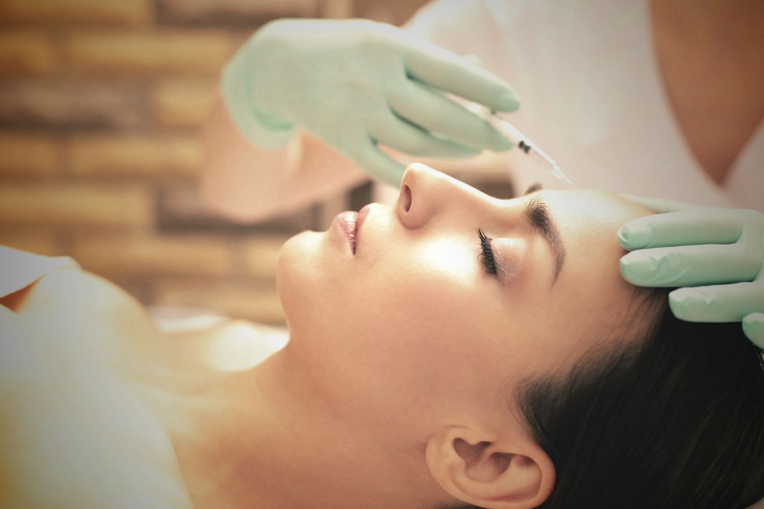 Woman receiving cosmetic injection in forehead by professional with gloves.