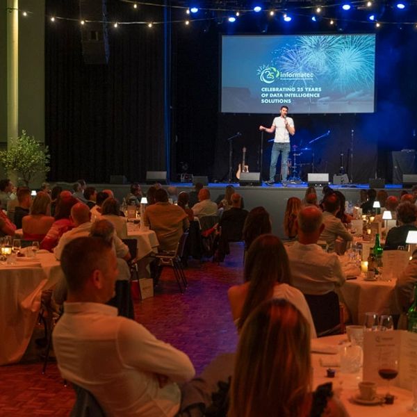 A speaker addresses an audience at a formal event with tables and lighting.