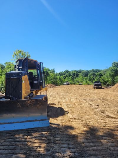John Deere 550K Bulldozer on Land Clearing site with exposed soil in the foreground. Blue Ford F350 