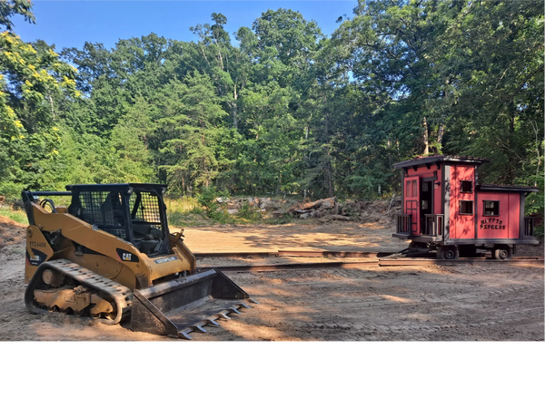 Caterpillar 259B3 Skidsteer with tooth bucket in front of cleared land with small red train caboose 