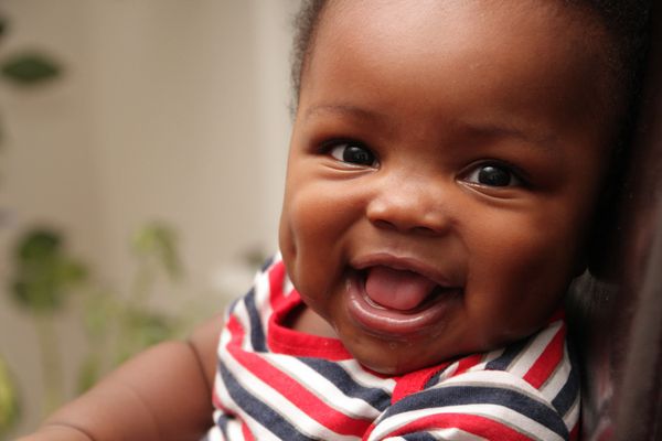 Happy baby smiling with dimples and wearing a striped shirt.
