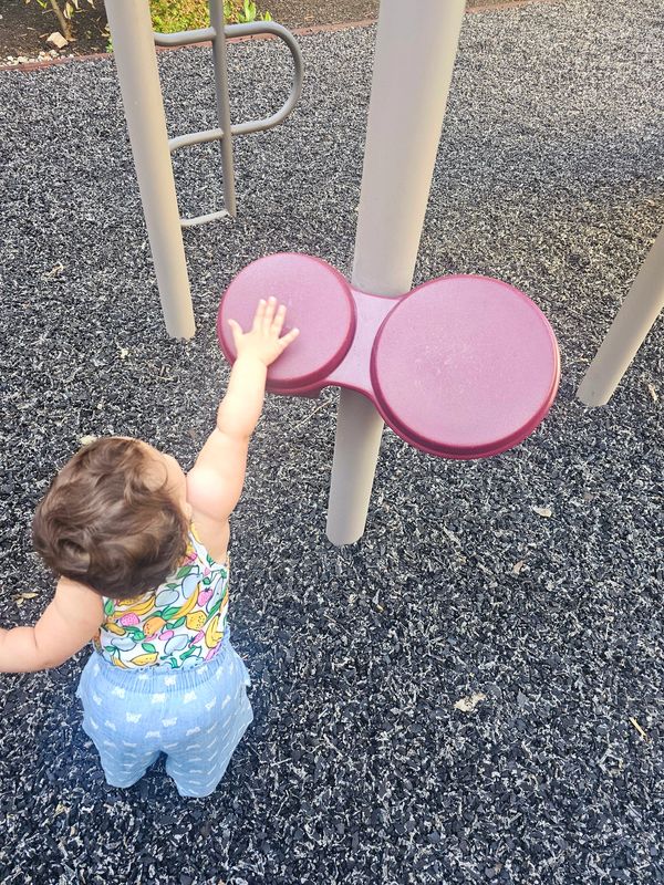 A toddler reaching up to touch playground equipment outdoors.
