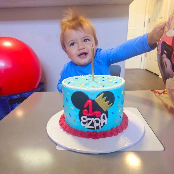 Happy baby celebrating first birthday with a colorful cake and balloons.