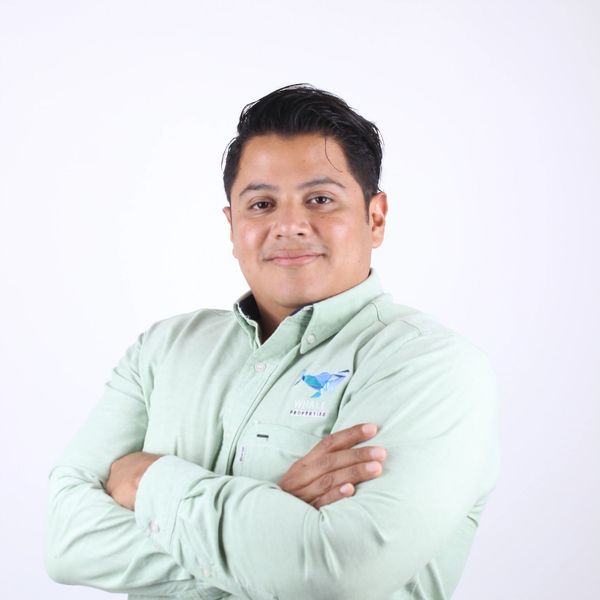 Hombre sonriente con brazos cruzados y camisa verde.