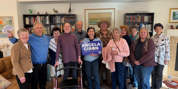 Group of people holding an Angela Giron sign indoors.
