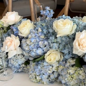 Elegant table centerpiece with blue hydrangeas and cream roses.