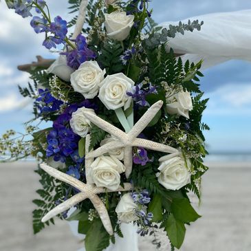 Beach-themed floral arrangement with white roses, purple flowers, and starfish.