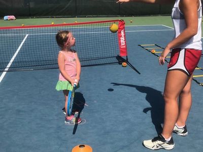 A young girl holding a tennis racket listens to her coach on a tennis court.