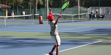 Young boy serving a tennis ball on an outdoor court.