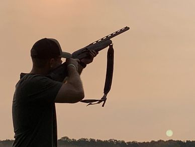 Man aiming a shotgun at sunset in a natural setting.