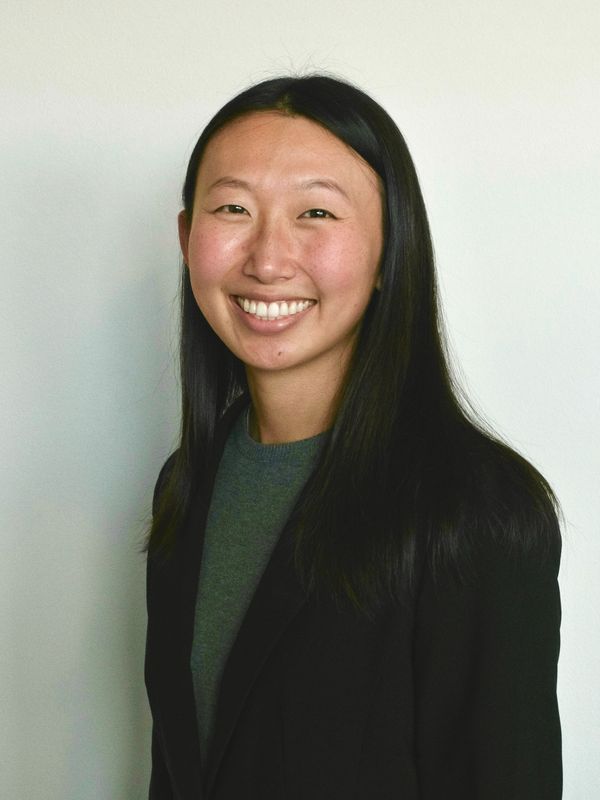 Smiling woman with long black hair wearing a black blazer and gray top.