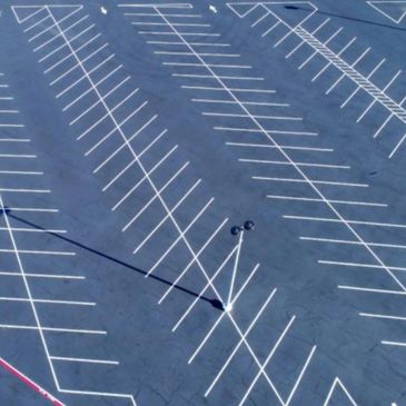 Empty parking lot with white lines and a single light pole casting shadows.