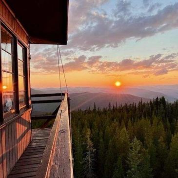 Sunset view from a wooden balcony overlooking forested mountains.
