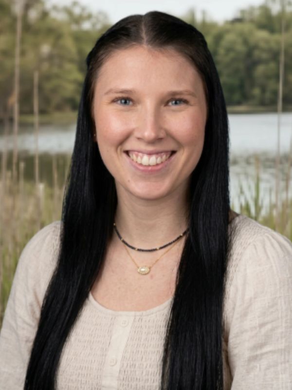 Smiling woman with long black hair by a lake.