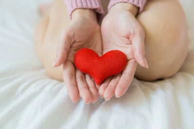Hands gently holding a small red heart symbol on a bed.