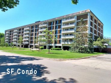 Large modern condominium building with balconies and green surroundings under a clear blue sky.