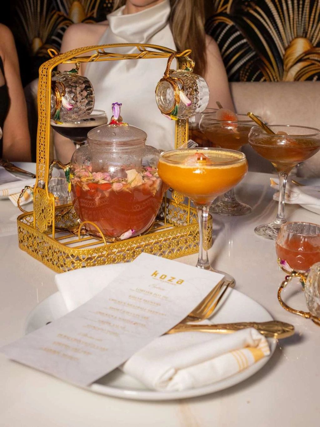 Elegant tea set with floral infusion and cocktails on a dining table.