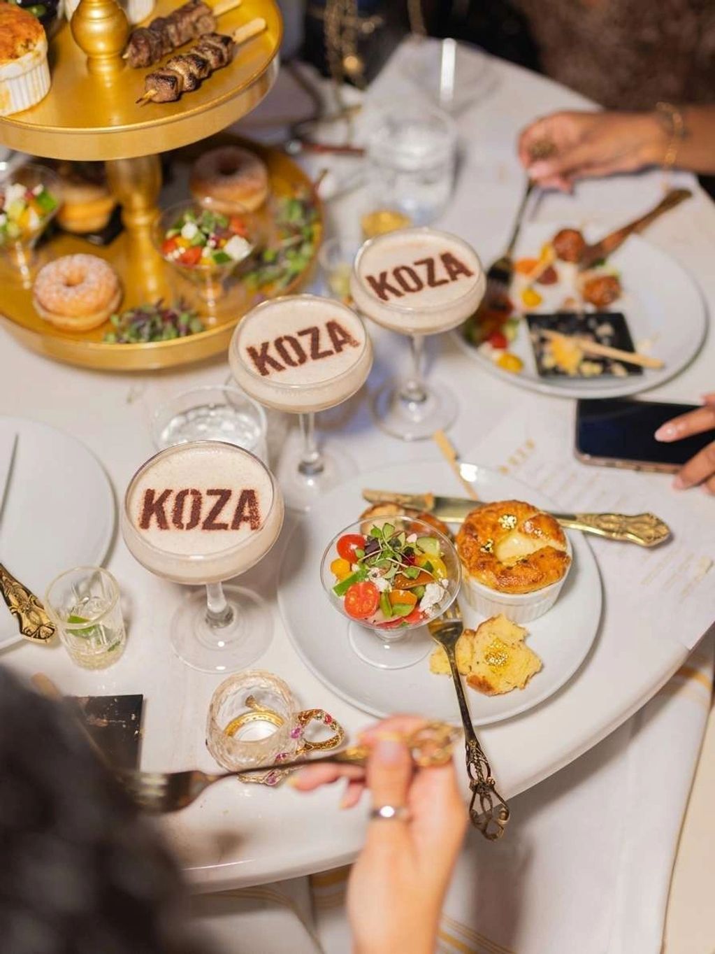 Elegant dining setup with cocktails labeled KOZA and gourmet appetizers.