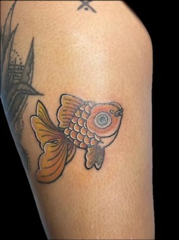 Colorful goldfish tattoo on upper arm with detailed scales and fins.