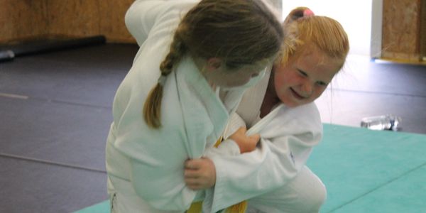 Two girls practicing judo on mats wearing white gi uniforms.