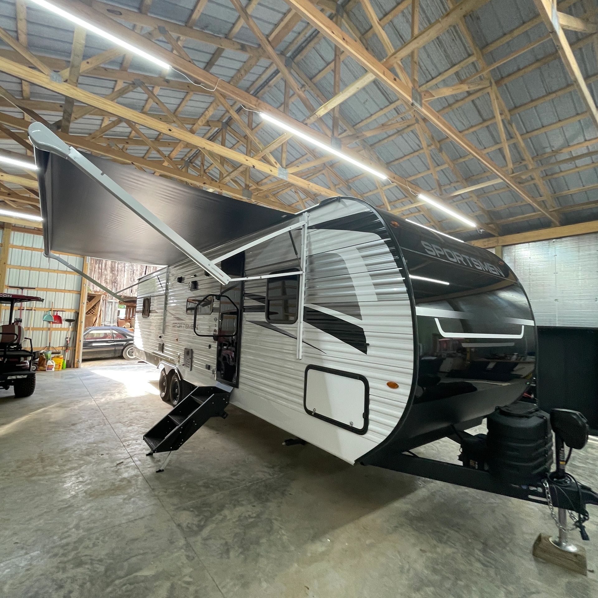 A recreational vehicle with an extended awning inside a wooden garage.