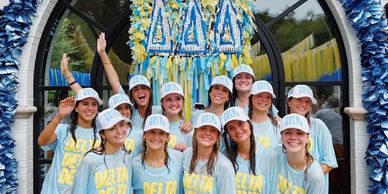 A group of smiling girls wearing Delta Zeta shirts and hats pose outdoors.