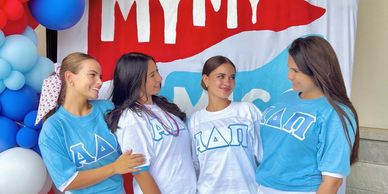 Four women in matching sorority shirts smile and chat at a decorated event.