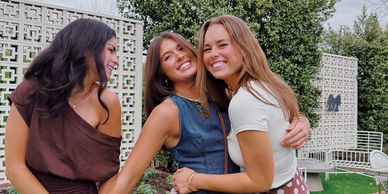 Three women happily posing together outdoors with smiles and embraces.