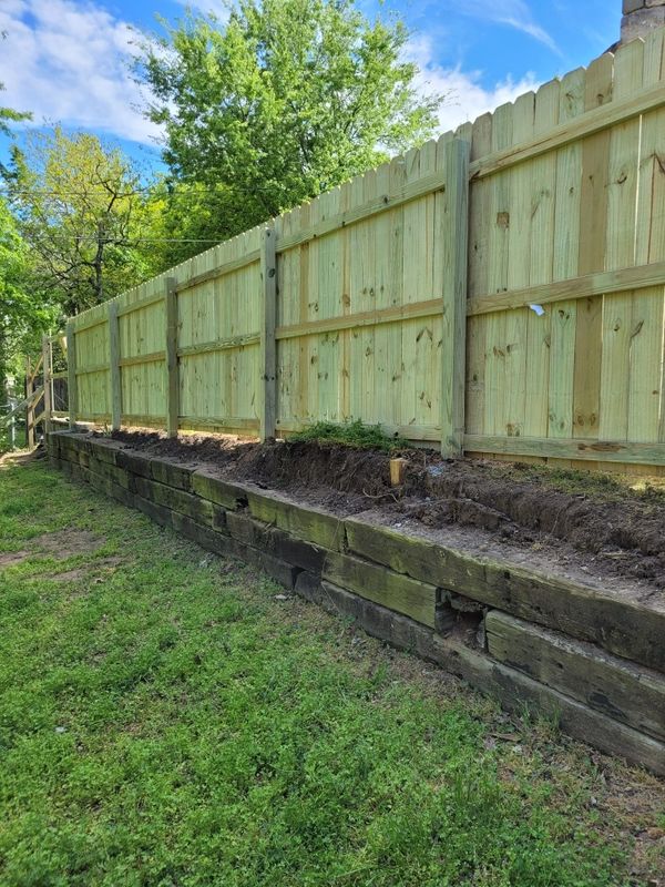 Wood privacy fence built on black retaining wall. 