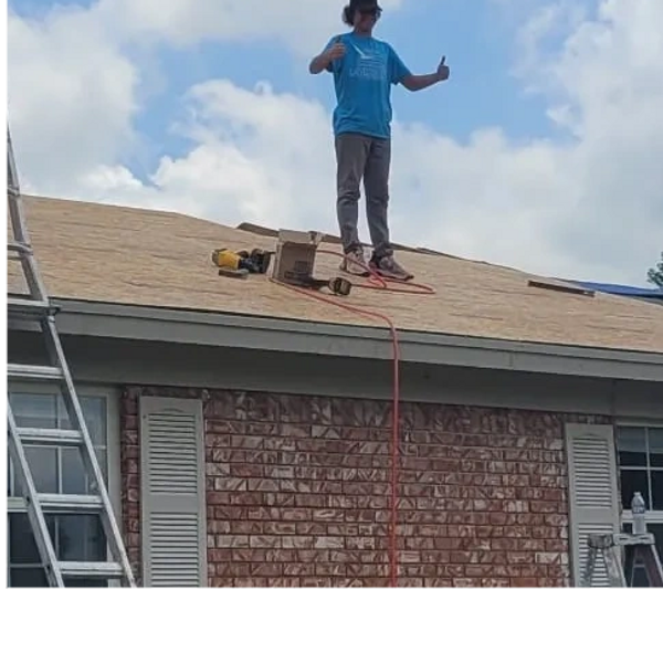 A teenager standing on a roof that has been repaired making the thumbs-up sign.