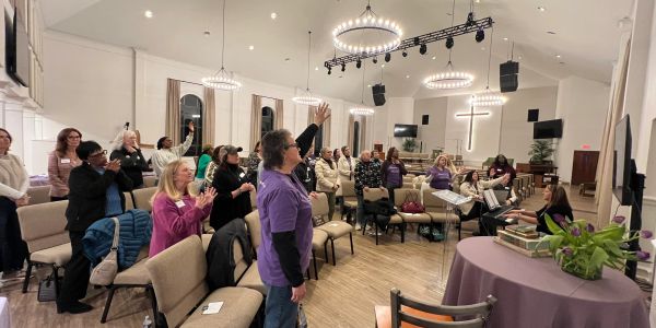 Group worship session inside a church with people raising hands and singing.
