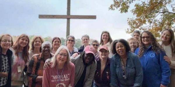 Group of women posing outdoors by a large wooden cross.