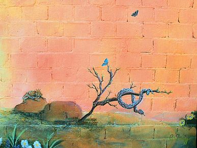 Mural on a brick wall. A spiney lizard sits on a rock watching a snake curl around a branch.