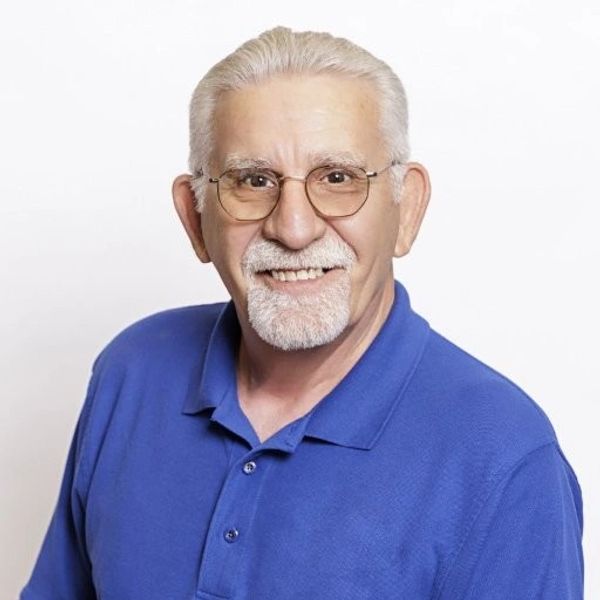 Smiling elderly man in glasses and blue polo shirt.