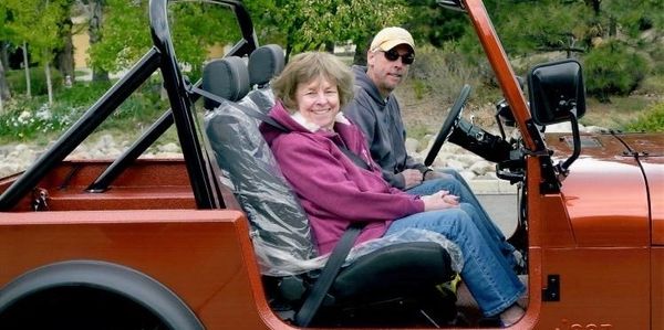 Two people sitting in an open-top orange vehicle, smiling and relaxed.