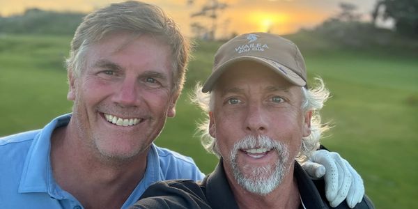 Two men smiling outdoors during sunset on a golf course.