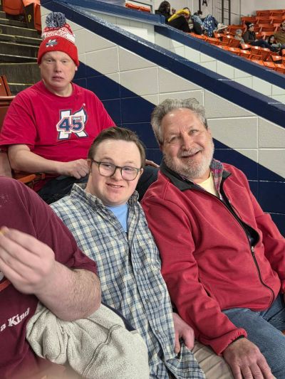 Three men sitting in stadium seats, smiling and relaxed.