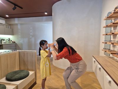 Woman helps girl try on glasses in a store.