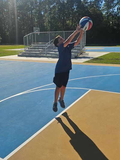 Boy jumping to catch a basketball on an outdoor court.