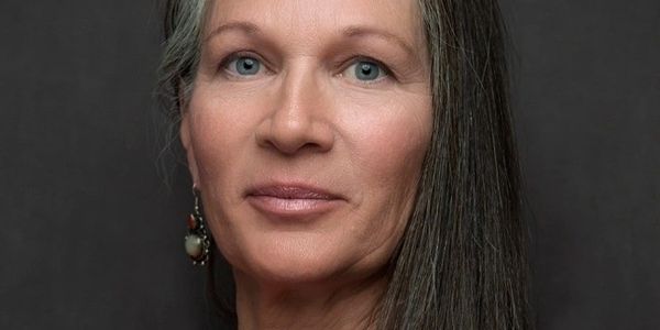 Portrait of a mature woman with long gray hair and blue eyes.