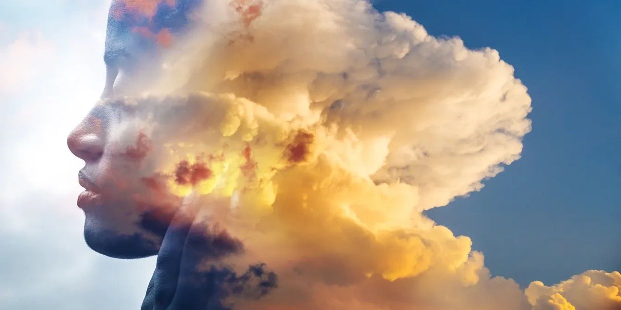 Double exposure of a person's profile blended with vibrant clouds at sunset.