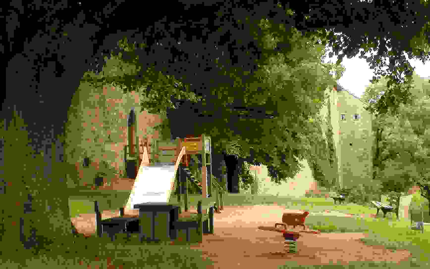 A climber with slide, a spring rider, and a picnic table with benches under a tree. 