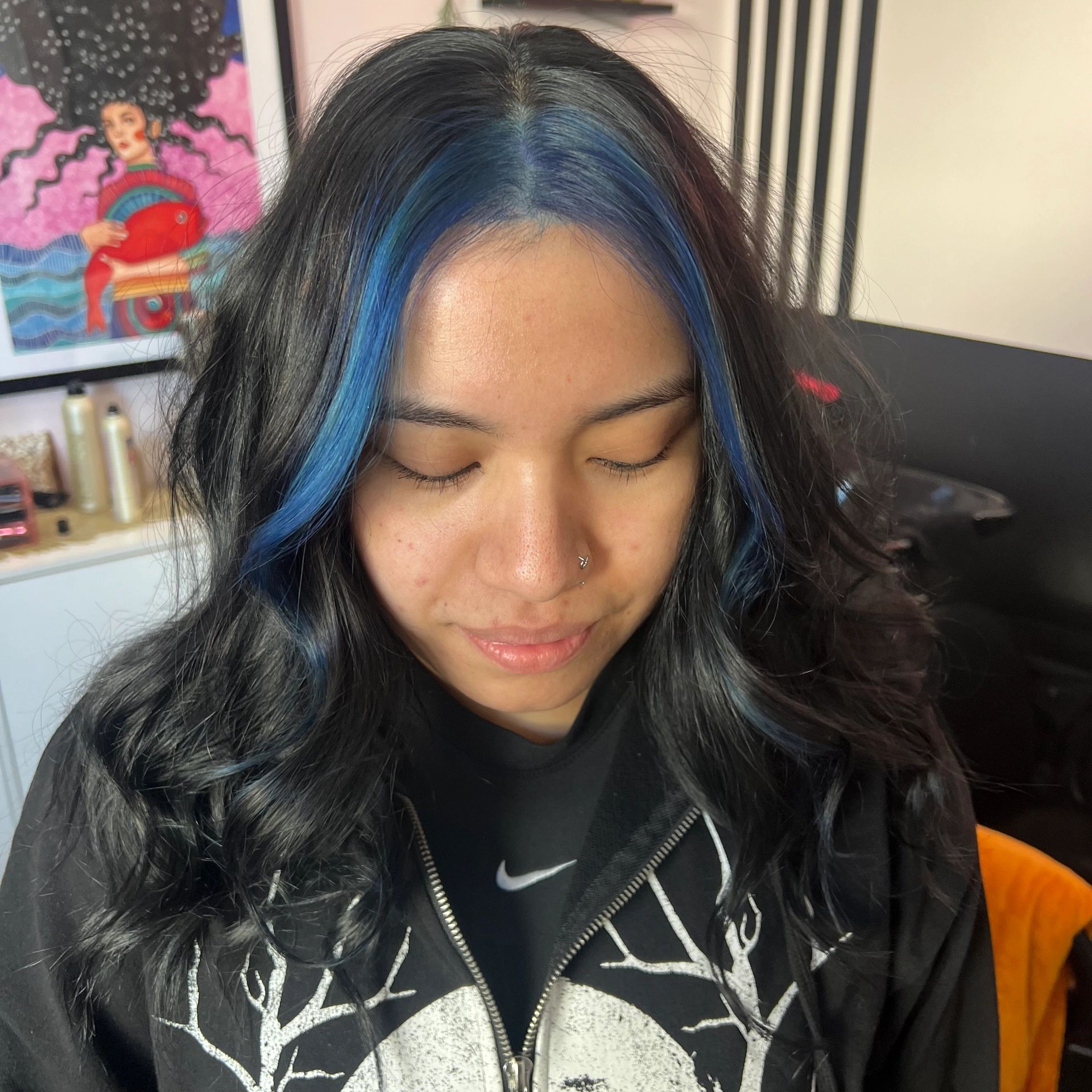 Young woman with black and blue hair looking down.