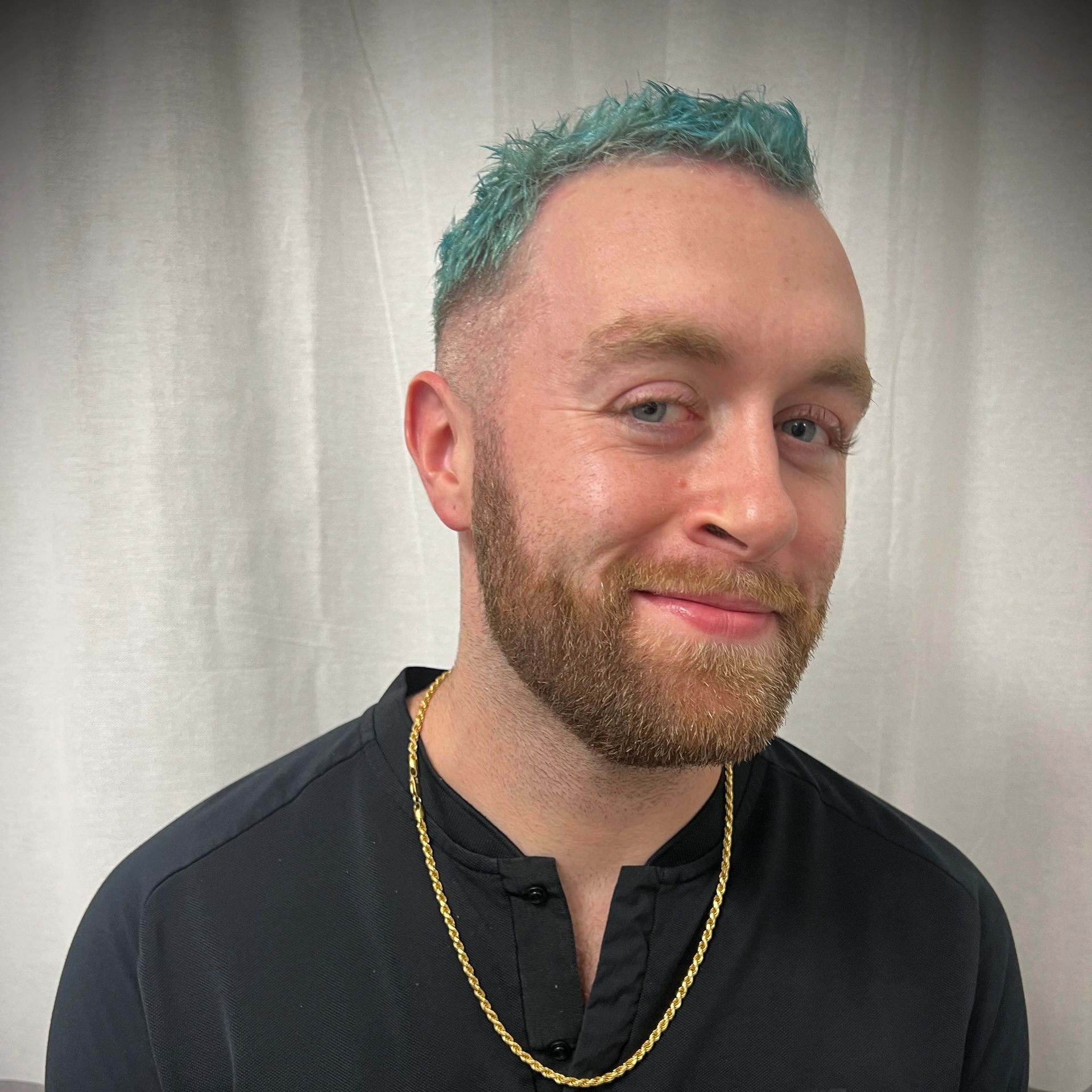 Smiling man with teal hair and gold chain.