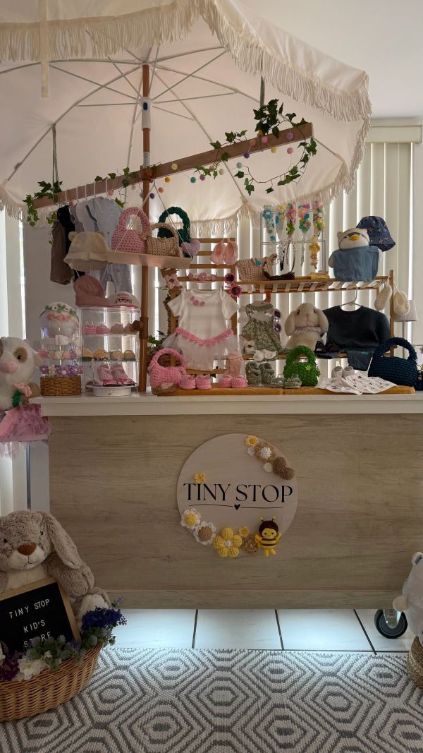 Cute kids' clothing and accessories displayed under a decorative umbrella at Tiny Stop.